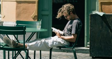 Homem lendo livro. Ele está sentando na cadeira de um café na rua