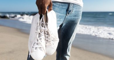 Homem caminhando na praia e segurando par de tênis branco