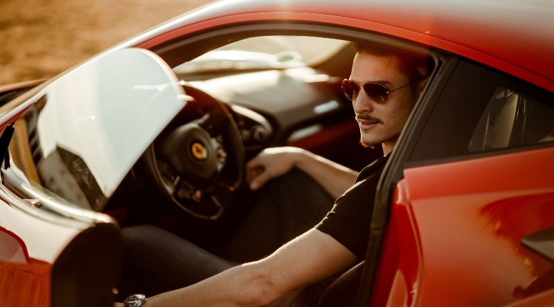 Carros e estilo: 5 combinações que definem o homem moderno 1 Homem de óculos escuros dentro de carro vermelho esportivo